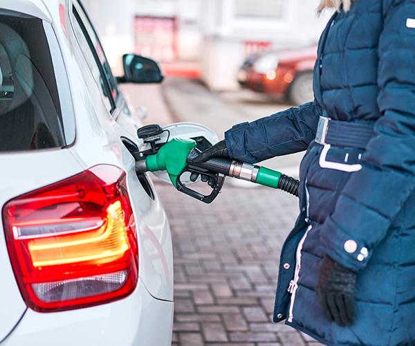 A person in a blue coat is filling up a white car with gas.