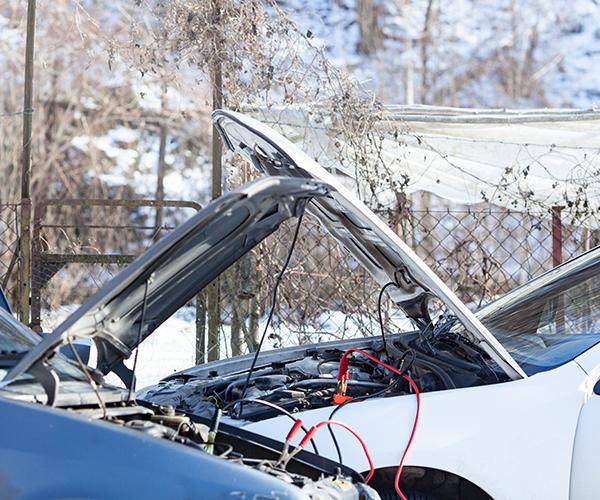 Two cars parked close to one another with both of the hoods open. Red and black jumper cables are connecting them.