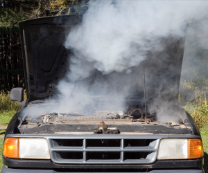 A truck with its hood open and smoke coming out from the engine.