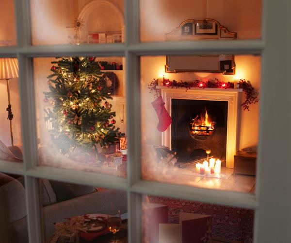 Through a frosted windowpane is a living room with a decorated tree, lit candles and a lit fireplace.