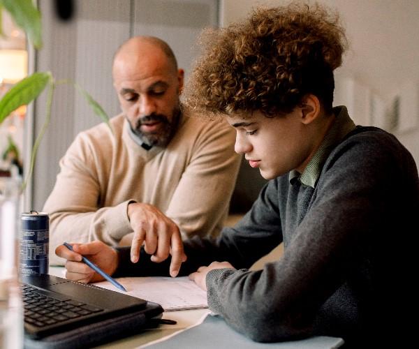 A parent helping their teenager with a form at a desk. 