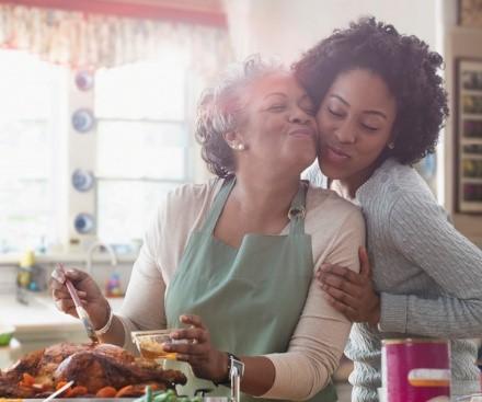 An individual preparing food while another individual is hugging them.