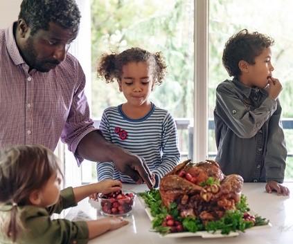 A man and three children placing cranberries around a platter with a cooked turkey on it.