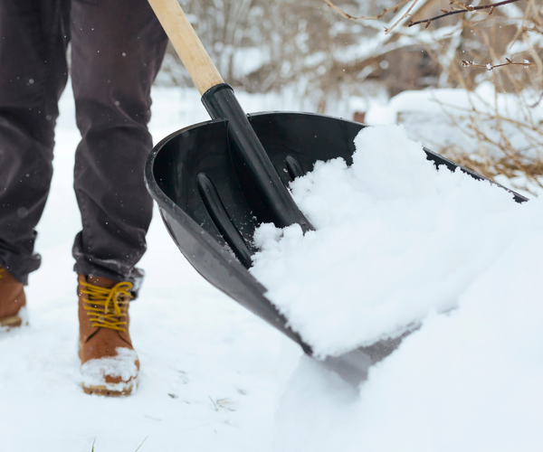 An individual shoveling snow wearing brown boots.