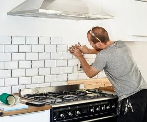 A contractor installing white backsplash tiles in a home kitchen.