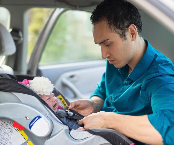 A person holding the buckle and straps of a car seat with a baby in it.