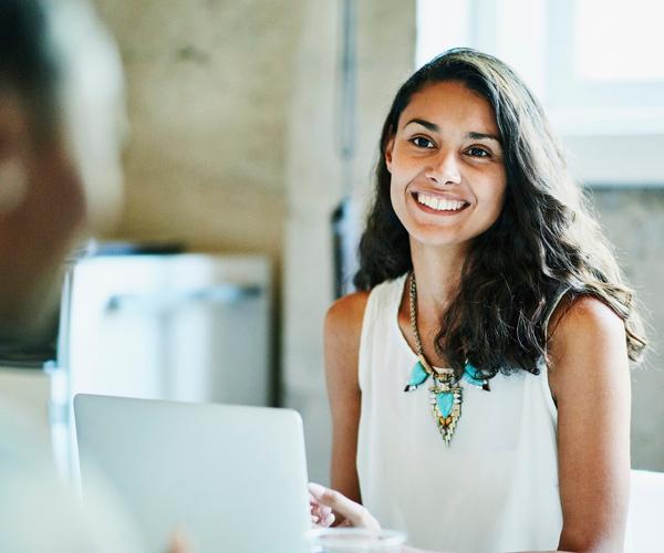 A person seated behind a laptop with a person across from them in an office.