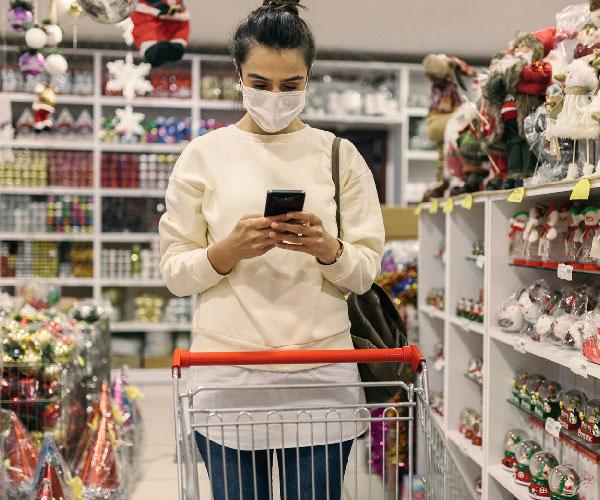 A person is holding a phone in their hands standing in front of a shopping cart in an aisle of decorations.