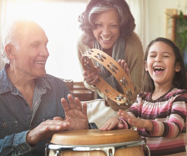 Two people are tapping a wooden drum while the third person is standing in between them holding a tambourine.