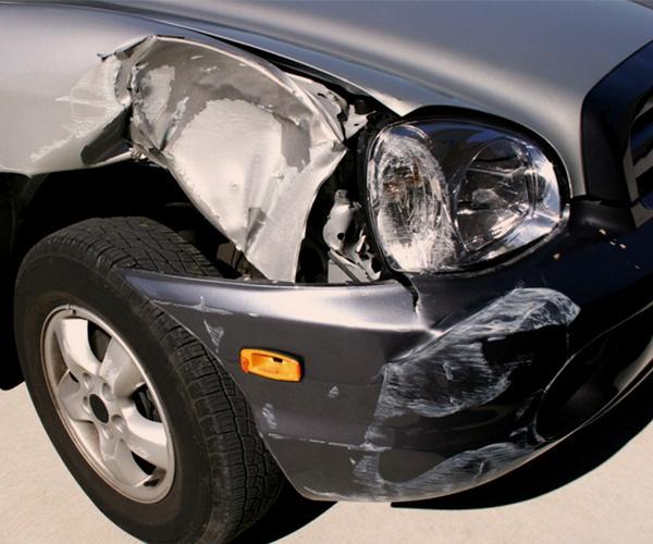 The front of a gray sedan with damage to the front bumper, headlight and front fender.