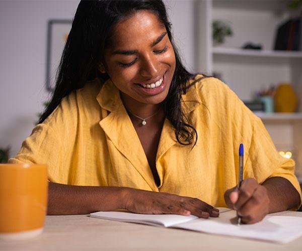 Person in a yellow shirt seated at a table writing in a notebook.