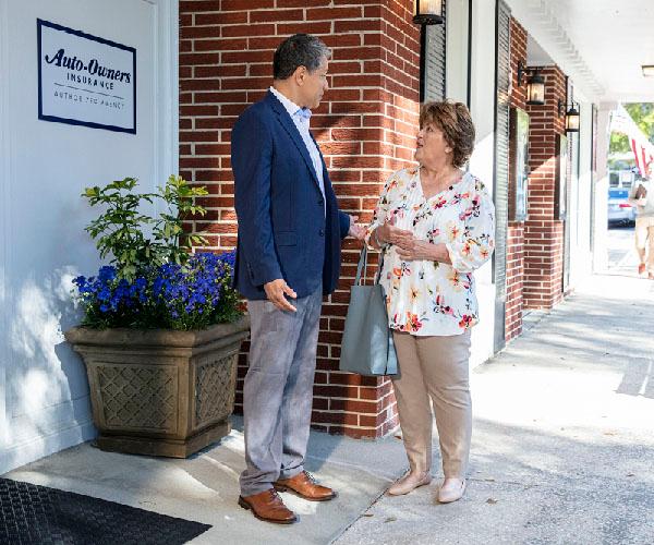 Two people engaging in a conversation outside of a brick building.