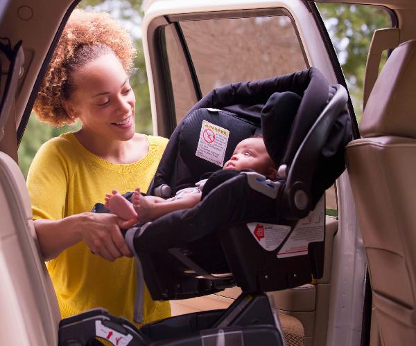 A person holding a car seat with a baby in it in the backseat of a vehicle.