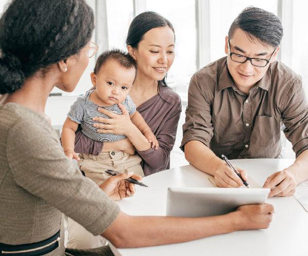 Three people and a baby seated at a table with two of those people using pens to point at a tablet.