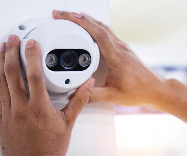 Two hands adjusting a white security camera on a wall.