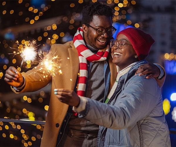 Couple dressed in warm clothing and holding sparklers outside.