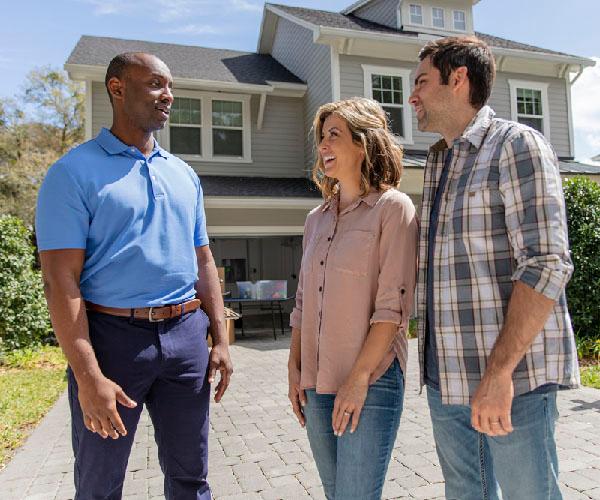 Three people talking on the driveway of a house.