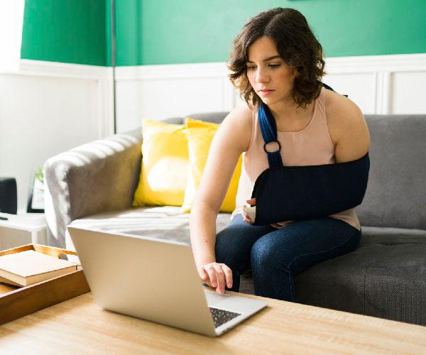 A person with an arm sling typing on a laptop after a having an accident and a broken bone.