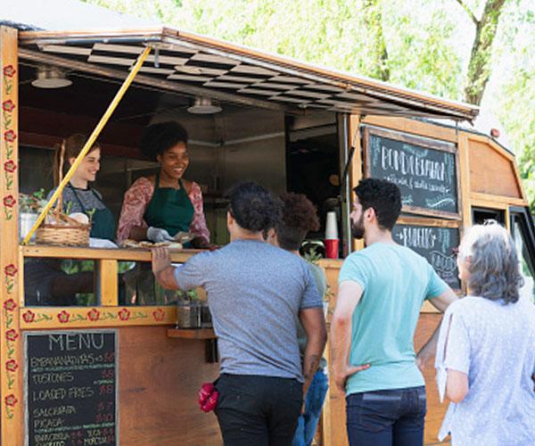 A food truck with it's bay window open and a line of customers lined up outside.