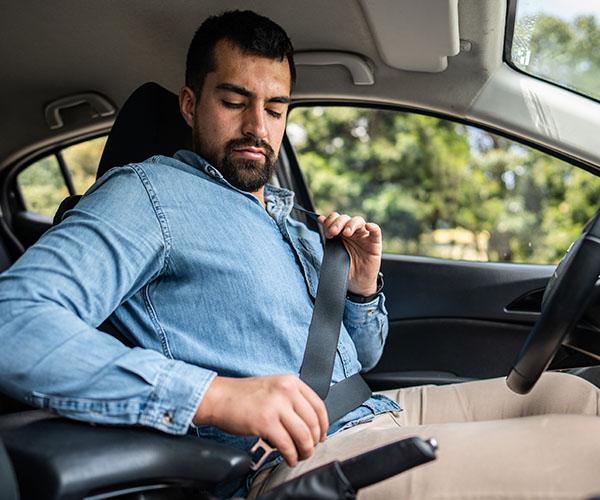 A person sitting in the driver's seat of a vehicle, pulling the seat best across their torso to fasten the seat belt.