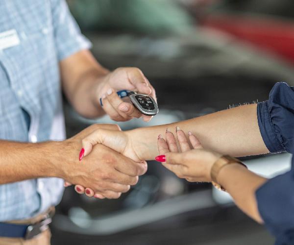 A person handing a car key fob to another person while they shake hands.