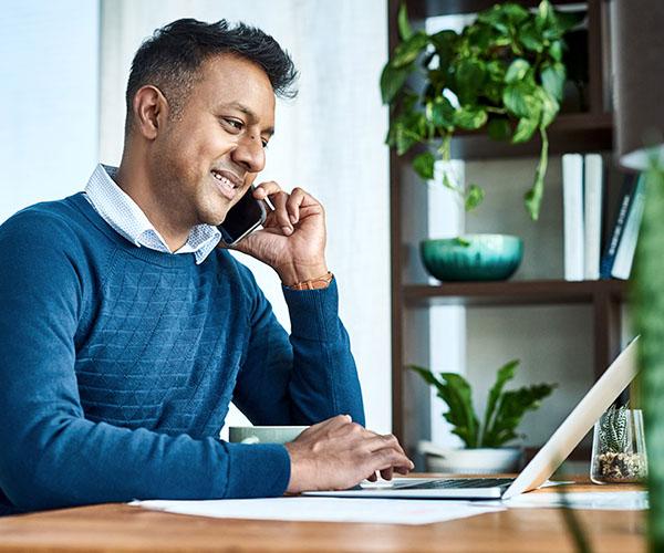 A person wearing a blue sweater on the phone while typing on a laptop.