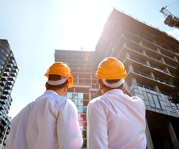 The back of two construction workers looking up at a building with scaffolding.