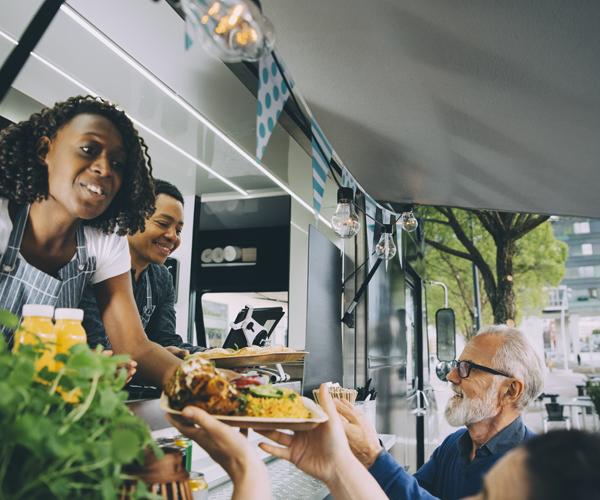 Two individuals working out of a food truck handing a plate of food to customers.