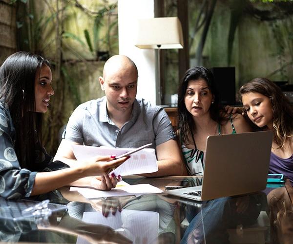 Four people sitting at a table looking for a laptop and papers.