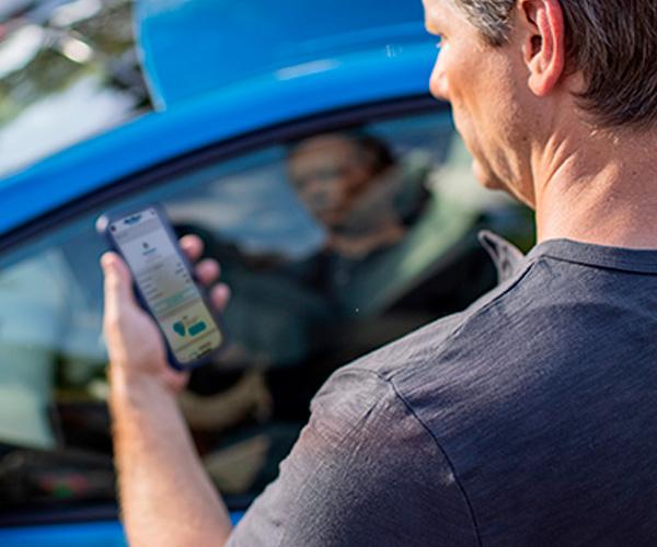 An individual checking their car insurance declaration on their phone in front of a blue sedan.