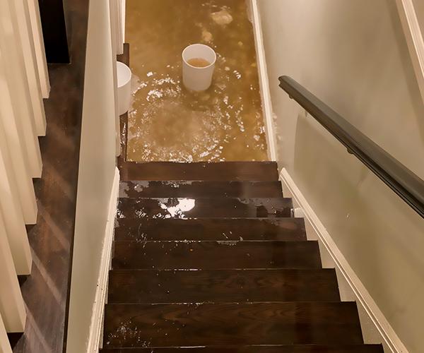 The bird's-eye view of a wet staircase leading to a flooded basement with a bucket at the bottom.