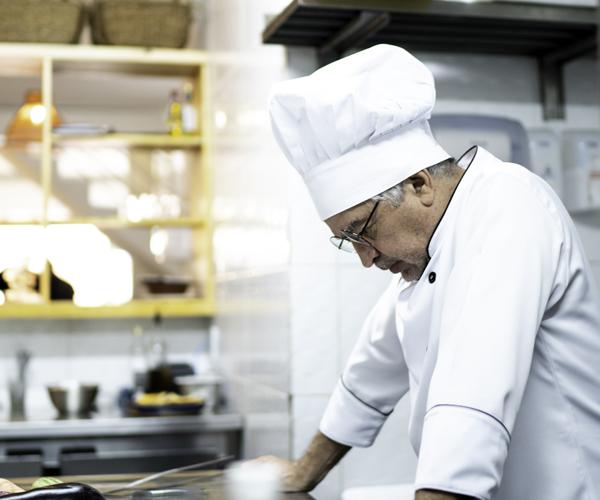 A chef in a commercial kitchen looking down with hands on counter.