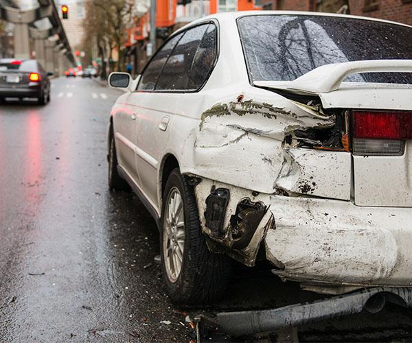 A white sedan parked in the road with rear bumper damage.