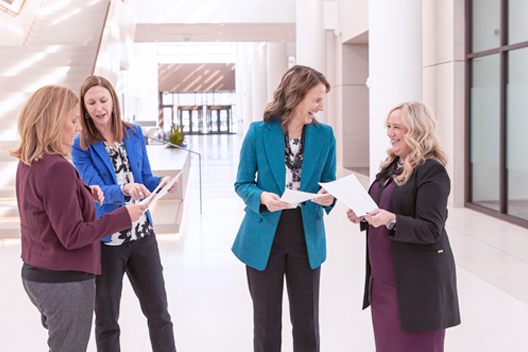 Four individuals each holding a piece of paper talking to each other.