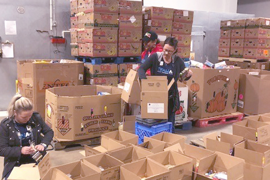 Three individuals in a warehouse surrounded by open cardboard boxes and organizing the contents. 