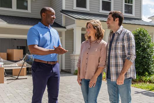 Three individuals talking to each other in front of a house on a driveway.