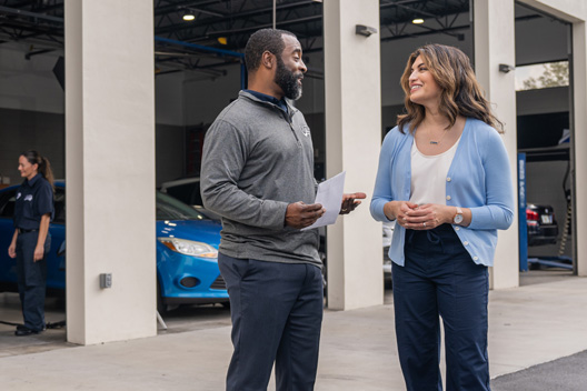 Two individuals conversing in front of an auto shop.